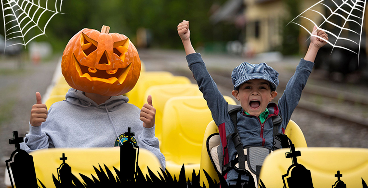 Two kids in Halloween costumes on railbike with pumpkin head and cheering.