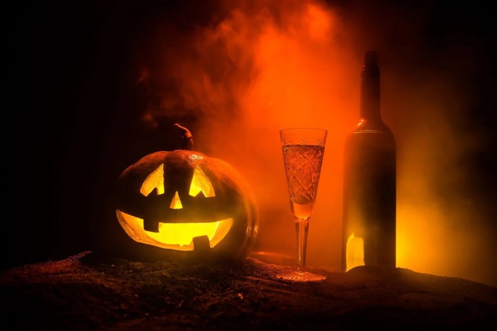 Jack-o'-lantern, wine glass, and bottle in smoky orange light.