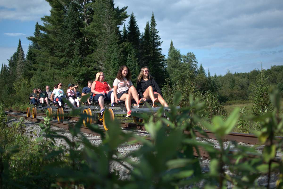 Group riding pedal-powered rail cars through forest landscape.